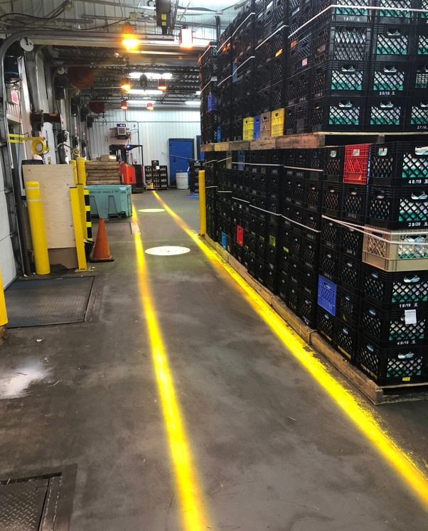 Bright amber lines projected onto the warehouse floor for the directional guidance and safe zone demarcation