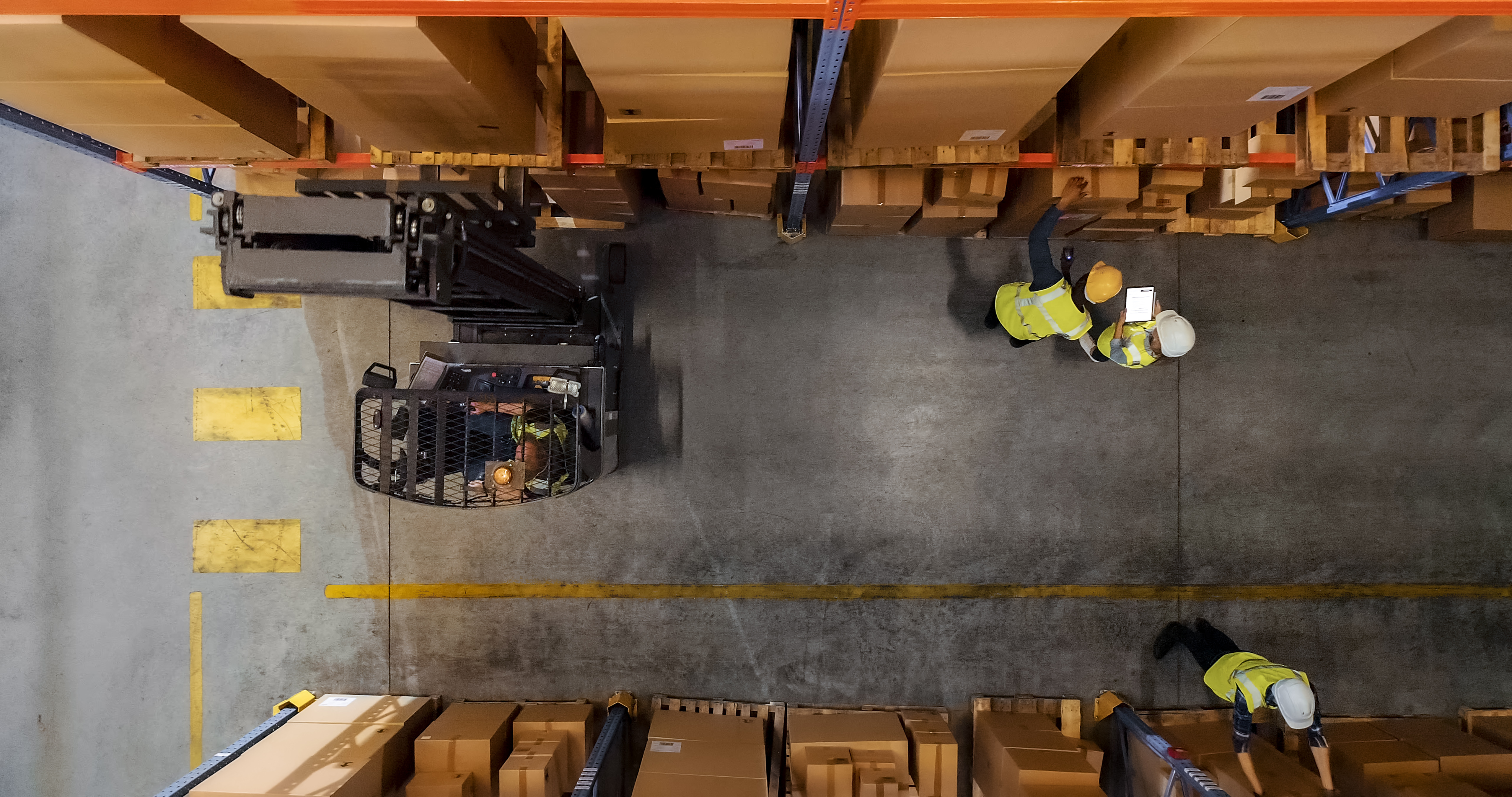 An overhead view of a warehouse aisle shows a forklift, three workers, and yellow floor markings between storage racks.